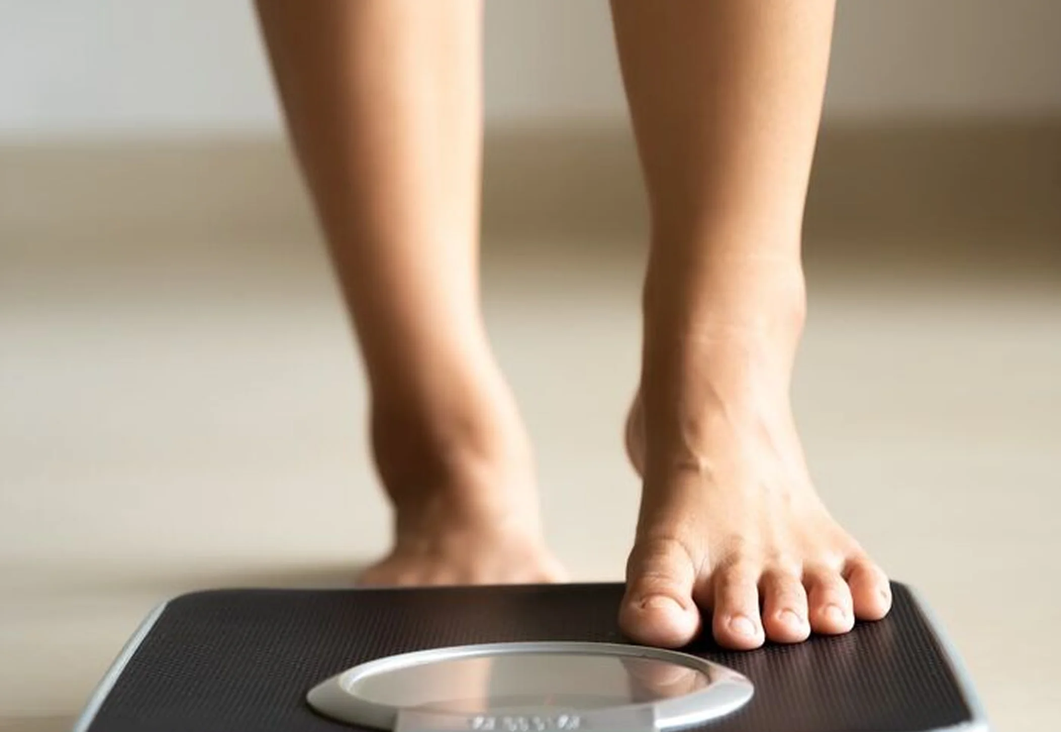 A woman wearing ¾ length leggings steps barefoot onto a set of digital scales.